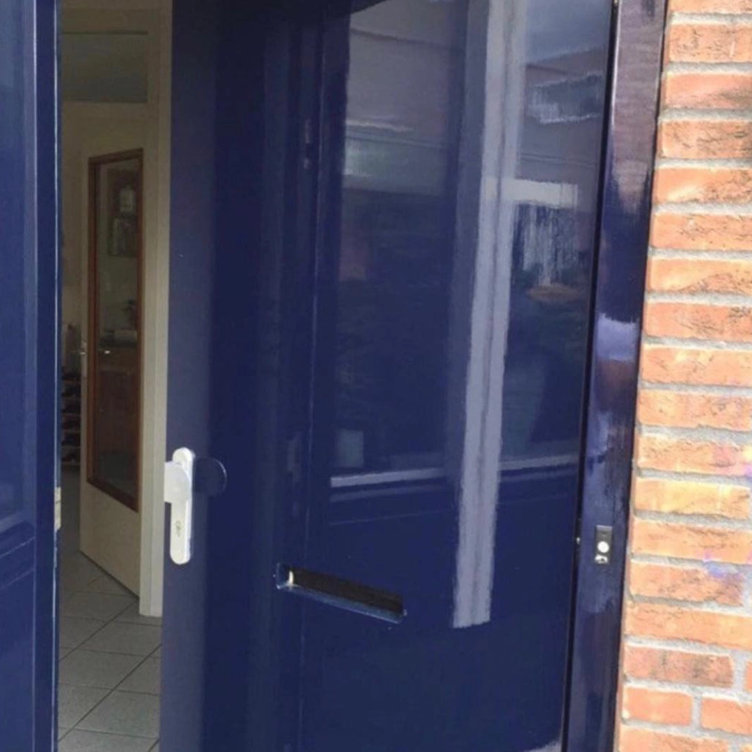 Hoogglans donkerblauw geschilderde voordeur met zilverkleurige greep en brievenbus, in een bakstenen gevel.