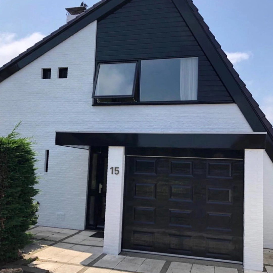 Vooraanzicht van een wit geschilderde woning met zwart houtwerk, zwarte garagedeur en kozijnen.