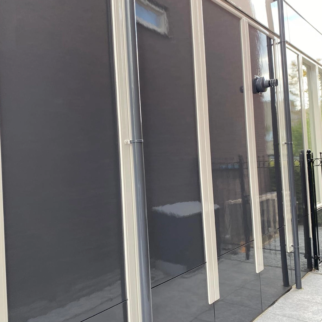Strakke donkergrijze gevelpanelen met witte afwerking en verticale regenpijpen.