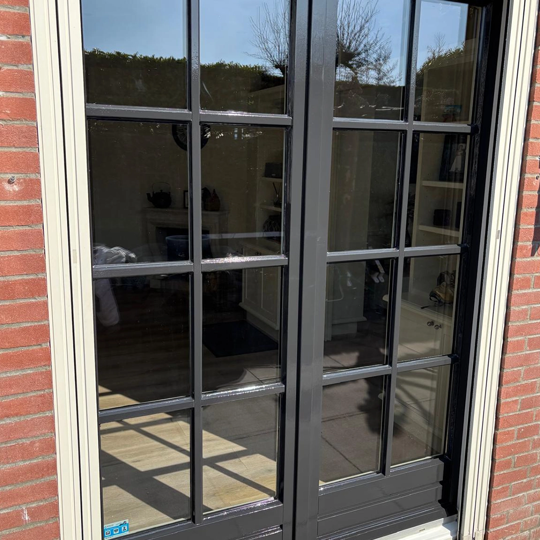 Detail van een zwart geschilderde openslaande deur met glaspanelen, omlijst door crème kozijnen.