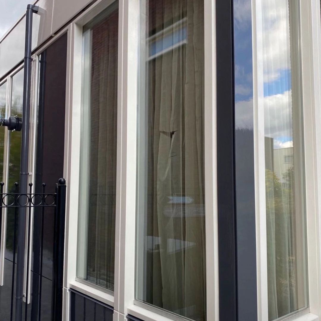 Witte kozijnen van grote ramen aan de buitenzijde van een woning, met reflectie van de lucht.