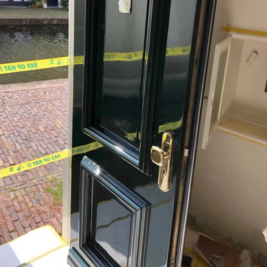 Donkergroen glanzend geschilderde voordeur met gouden deurklink, gezien vanuit binnen.