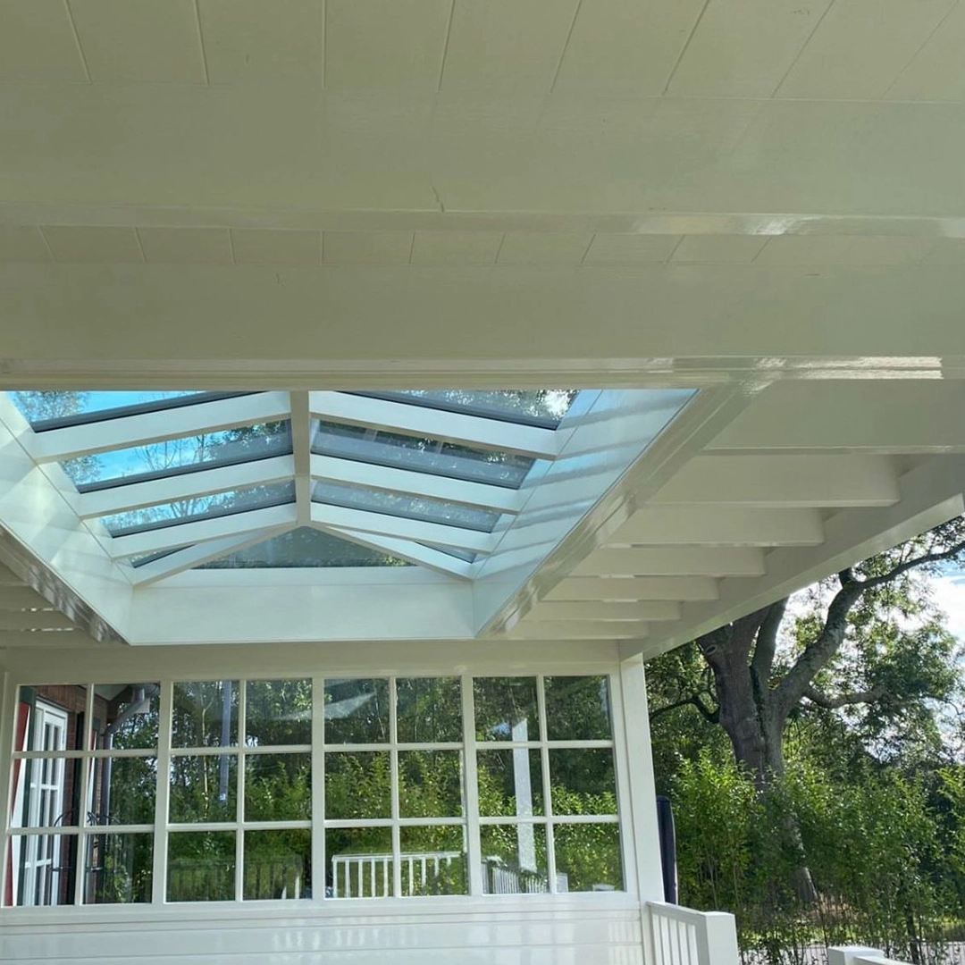 Wit geschilderde veranda met een zadeldak en glazen dakraam, met uitzicht op groene tuin.