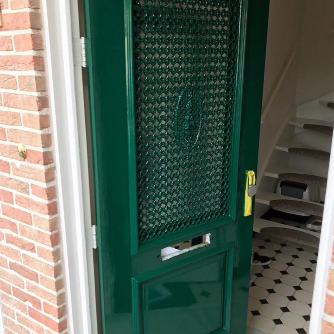Groen gelakte voordeur met sierrooster en glas, in een jaren 30-stijl.