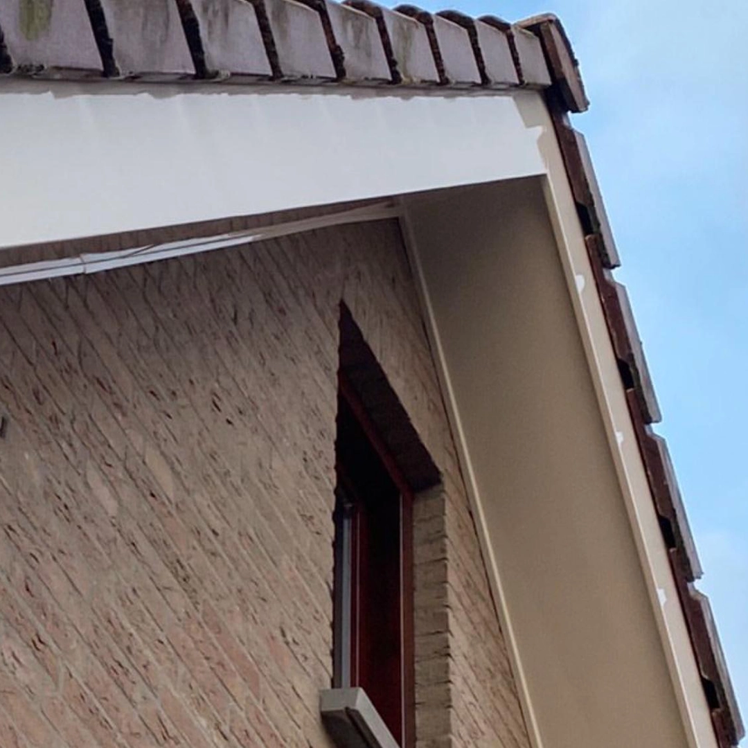 Fris geschilderde witte boeidelen onder een pannendak aan een gevel met rode bakstenen.