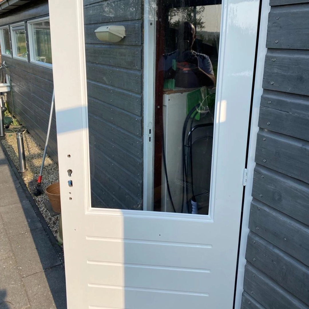 Strak wit geschilderde achterdeur met groot glasvlak, naast een grijze houten gevel.