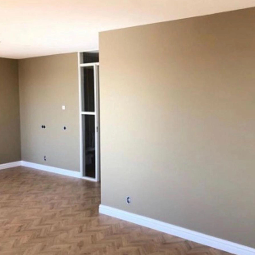 Strak geschilderde kamer met beige muren, witte plinten en een houten visgraatvloer.