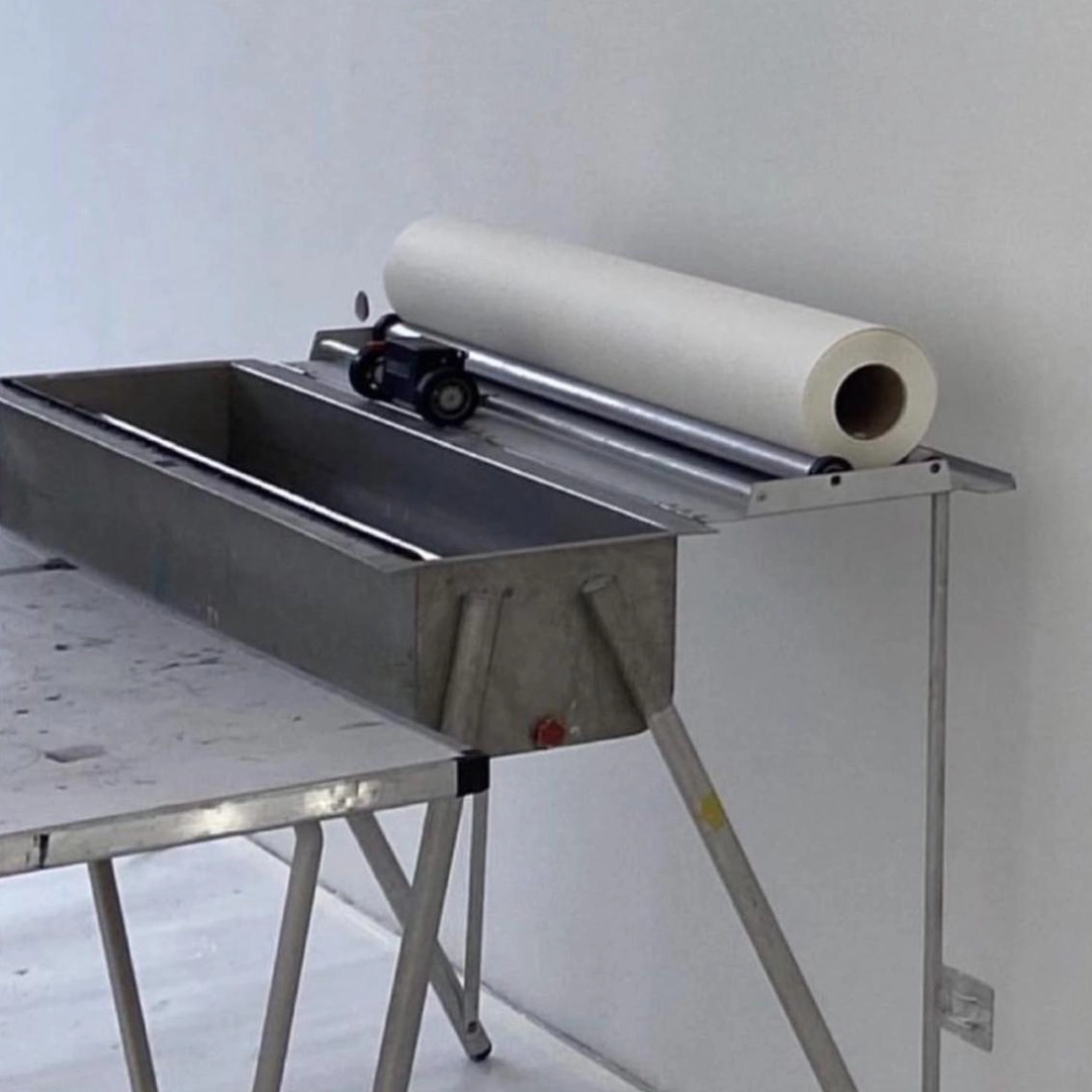 Aanbrengtafel met behangmachine en een rol glasvezelbehang, klaar voor verwerking op een strak afgewerkte witte muur.