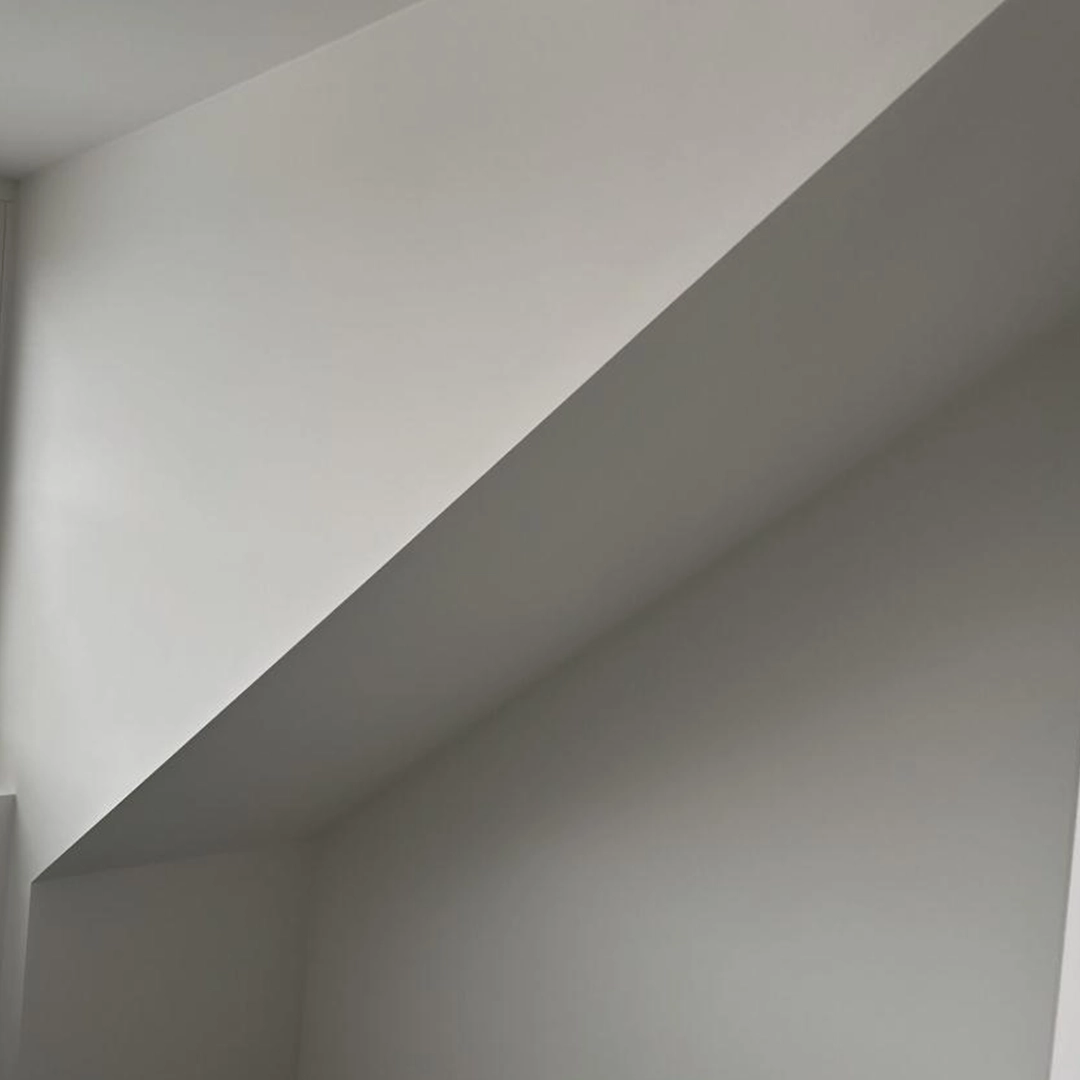 Strak wit gespoten schuine wand en plafond in een moderne ruimte met veel lichtinval.