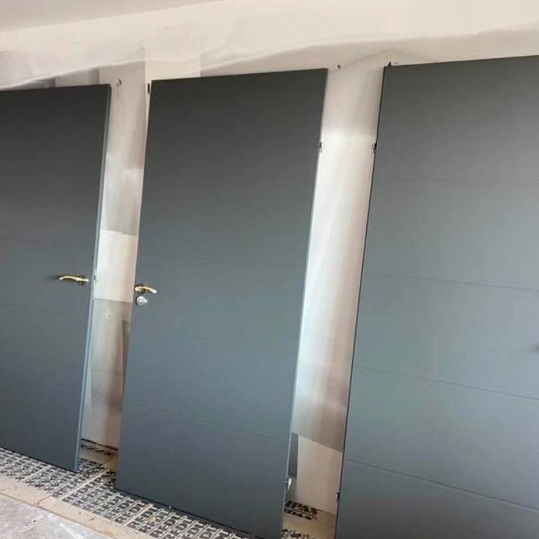 Drie strak gespoten binnendeuren in een matte, donkergrijze kleur staan rechtop te drogen in een zorgvuldig afgeplakte ruimte, klaar voor montage; de moderne afwerking en egale verflaag benadrukken het vakmanschap en de zorgvuldige voorbereiding.