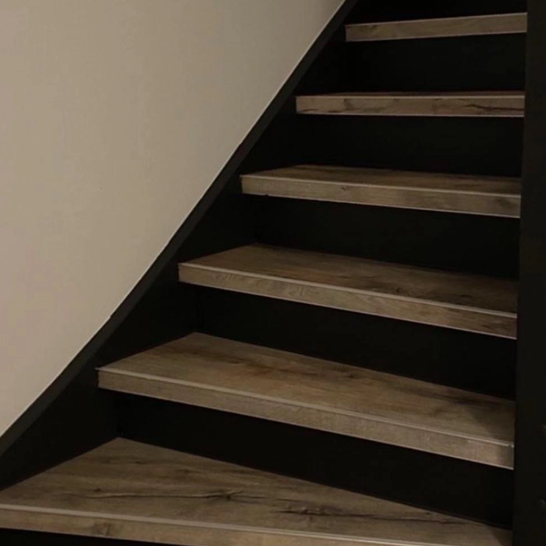 Deze trap is afgewerkt met een stoere combinatie van zwart en houtlook. De donkere zijkanten zorgen voor een krachtig contrast met de natuurlijke houttinten van de treden, wat een moderne en robuuste uitstraling geeft. Het geheel oogt strak, professioneel geplaatst en goed afgestemd op een interieur met industriële of minimalistische stijl. Een opvallende en stijlvolle keuze.