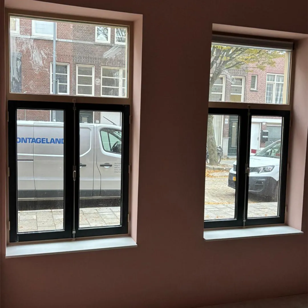 Twee zwarte-framed ramen met zicht op straat met een witte bestelwagen en een witte auto geparkeerd.
