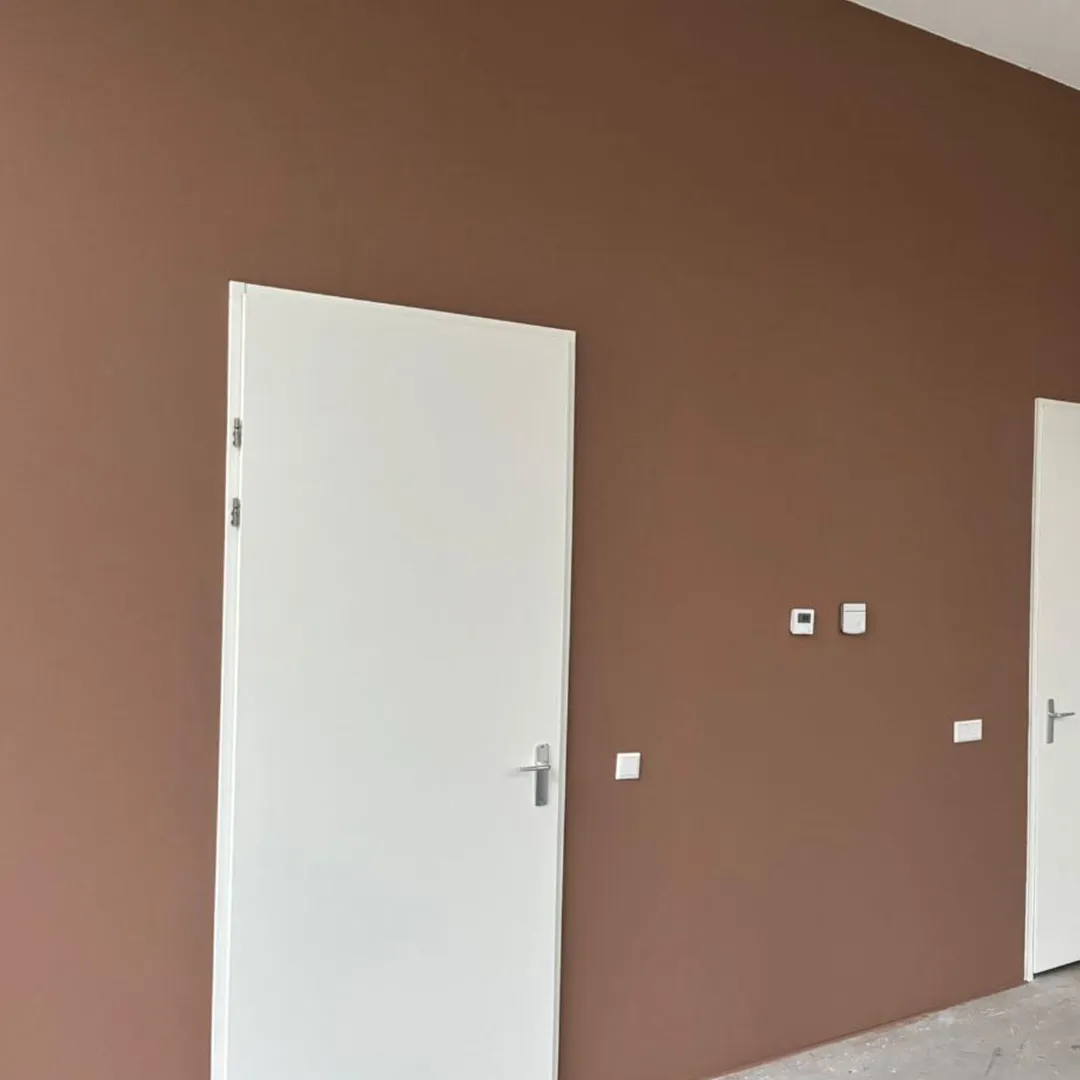 Bruine muur met twee witte deuren en drie schakelaars ertussen.