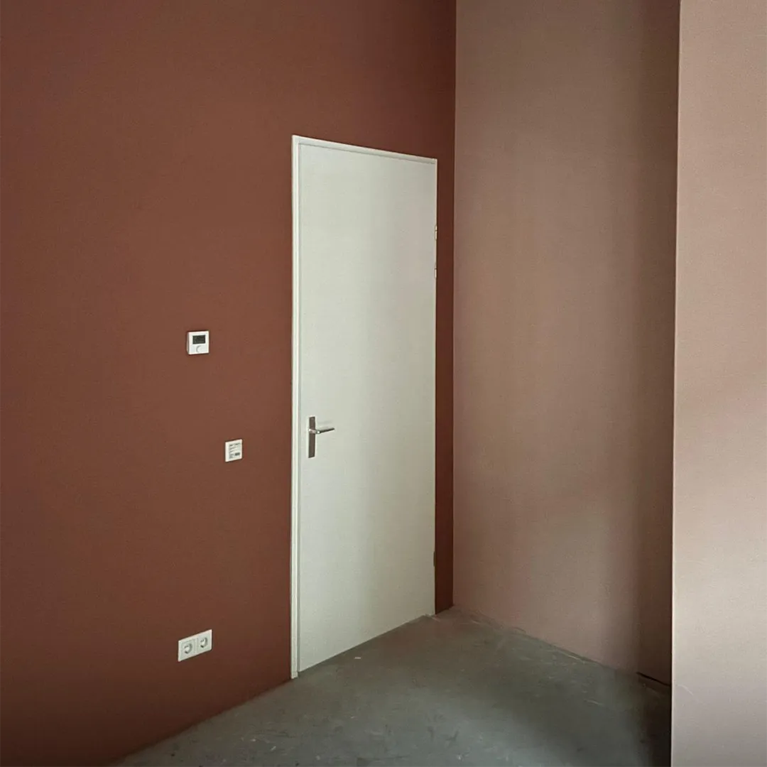 Witte deur in een kamer met muren in verschillende tinten bruin en een betonnen vloer.