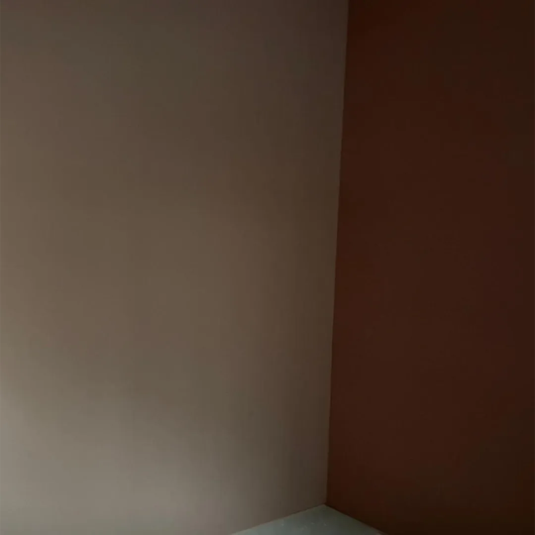 Hoek van een lege kamer met twee muren en een vloer met neutrale kleuren.