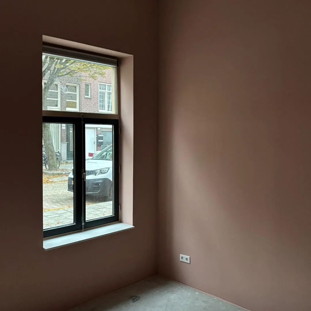 Leeg hoek van een kamer met een raam dat uitzicht biedt op een straat met een geparkeerde witte auto.