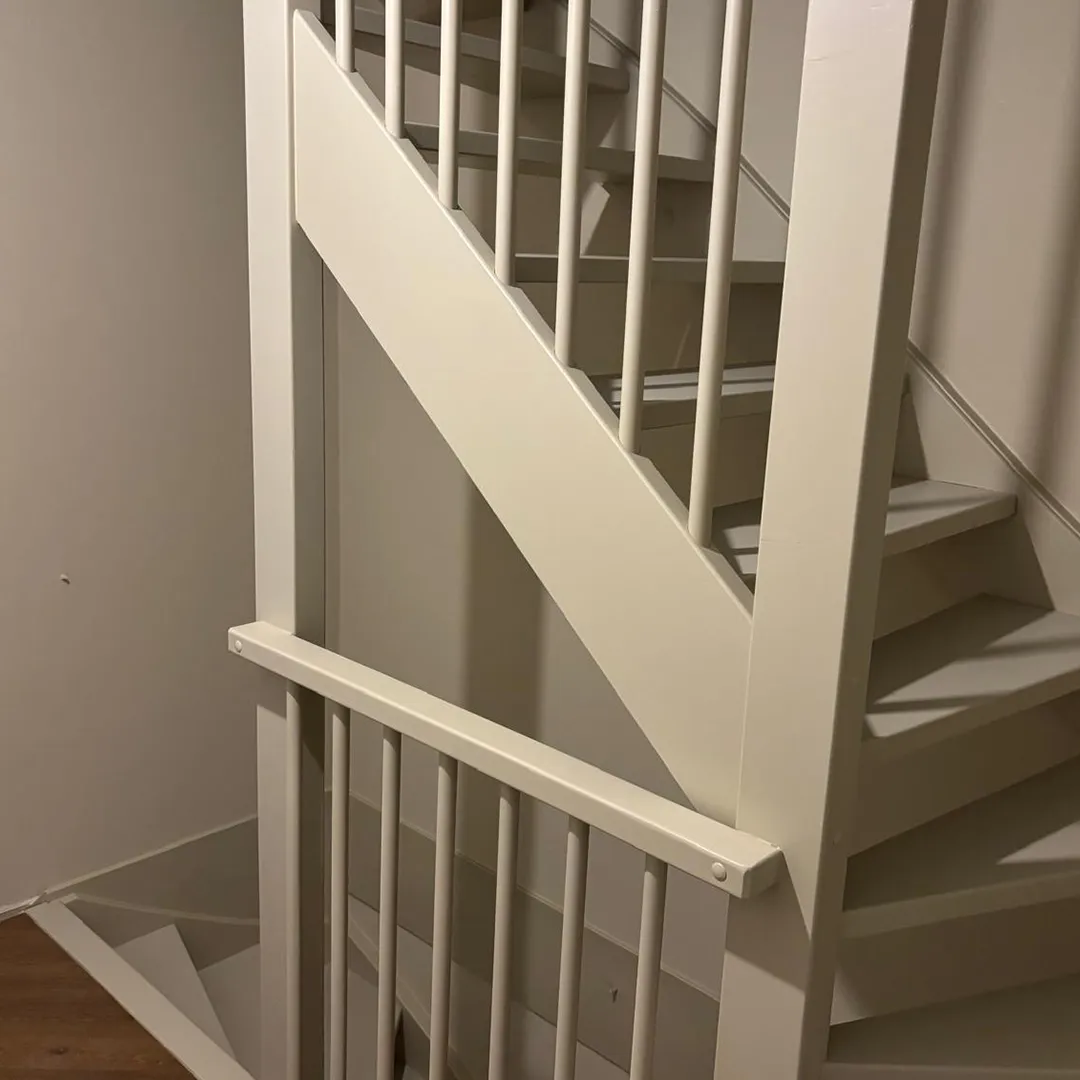 Witte trap met houten treden en spijlen binnen een woning.