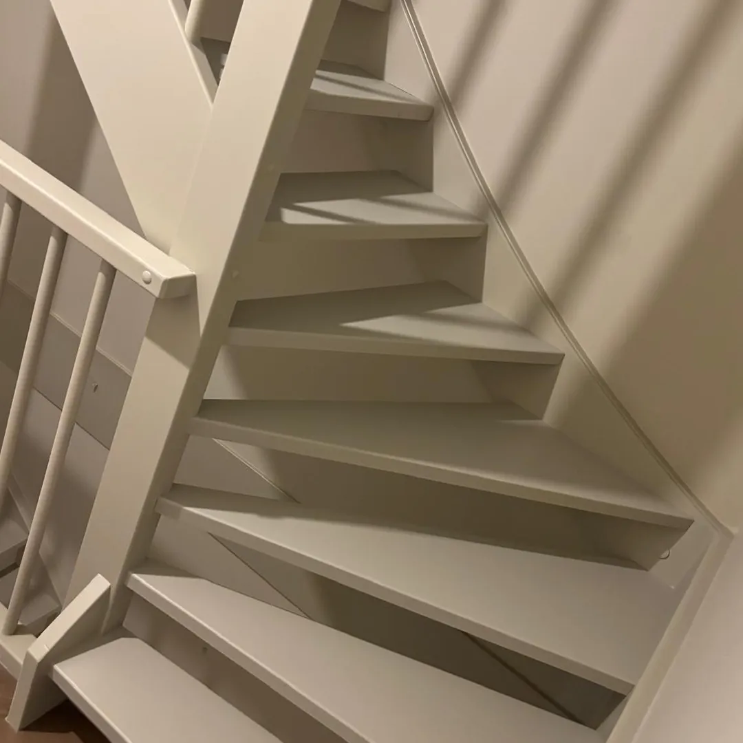 Witte open houten trap met leuning tegen een beige muur met schaduwpatroon.