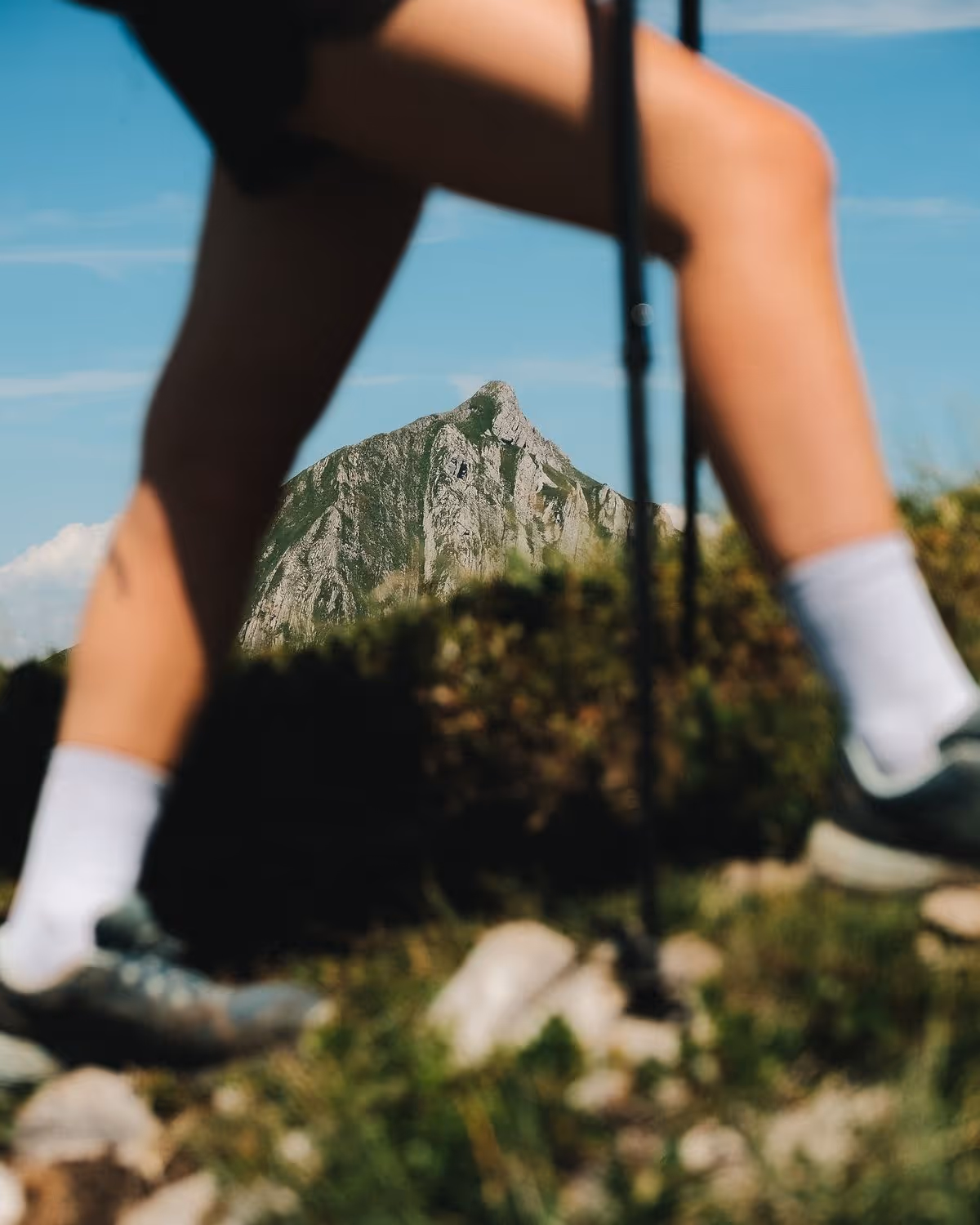 Jambes d’un randonneur avec bâtons de marche sur un sentier de montagne.
