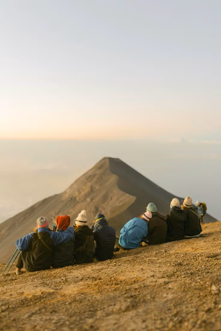 Groupe de randonneurs assis au lever du soleil face à un sommet volcanique.