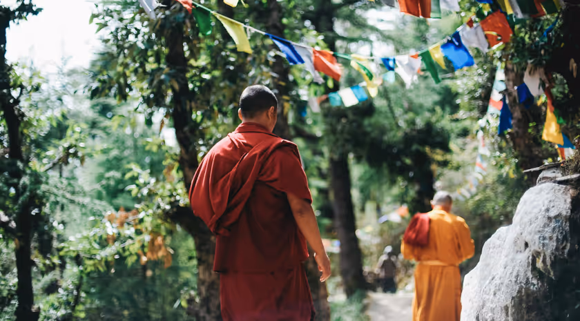 Moines bouddhistes en robe orange marchant sous des drapeaux de prières colorés.