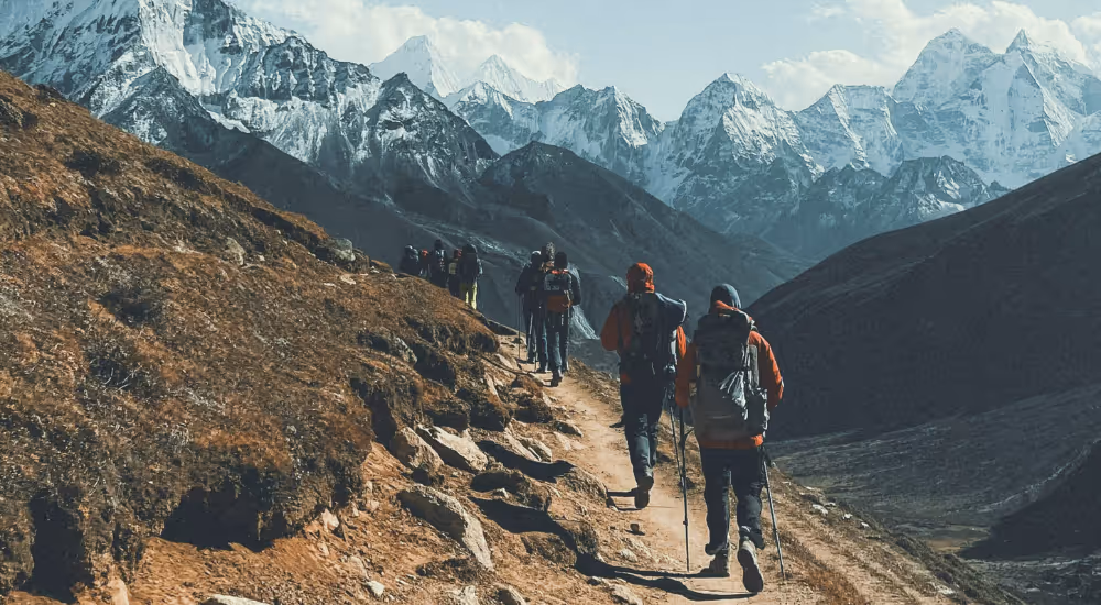 Groupe de randonneurs progressant sur un sentier himalayen avec sommets enneigés au loin.