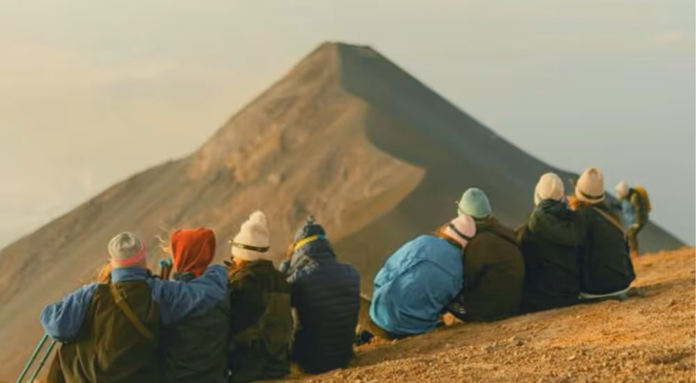 Groupe de voyageurs assis face à un volcan au lever du soleil.