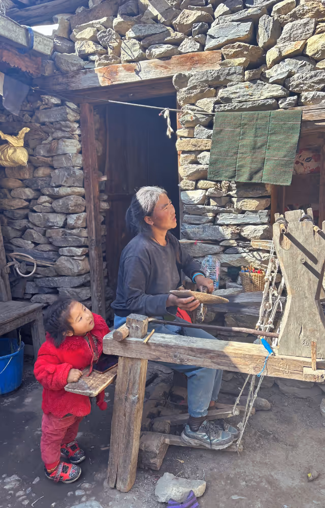 Femme népalaise qui tisse à la machine à main dans un village de montagne avec son enfant.