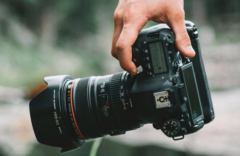 Main tenant un appareil photo reflex en pleine nature.