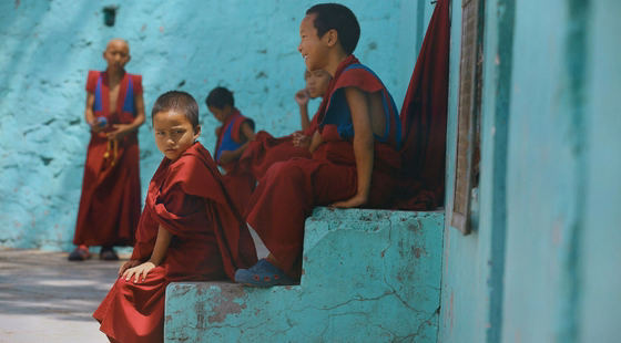 Enfants bouddhistes assis sur des marches devant un mur turquoise.