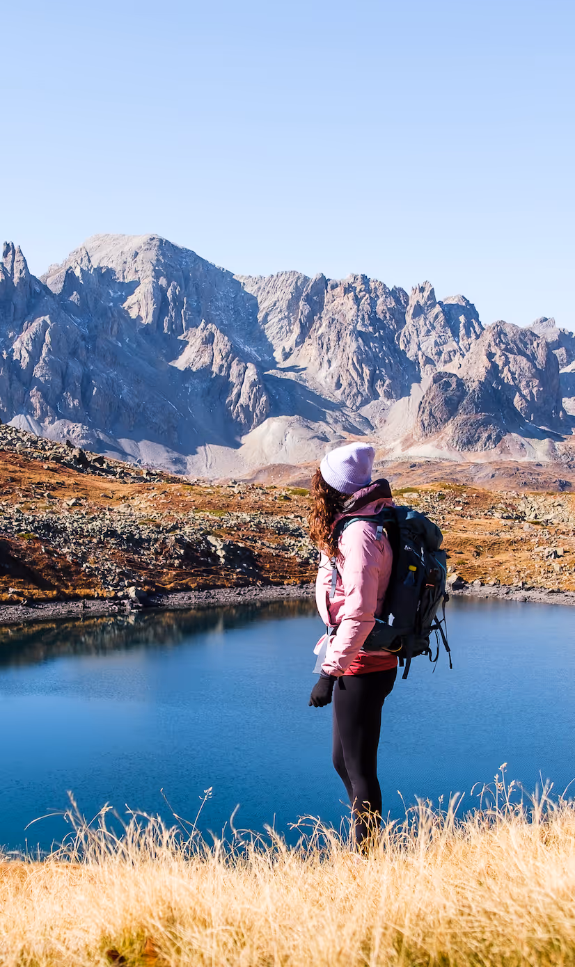 Femme observant un lac alpin entouré de montagnes dans les Écrins