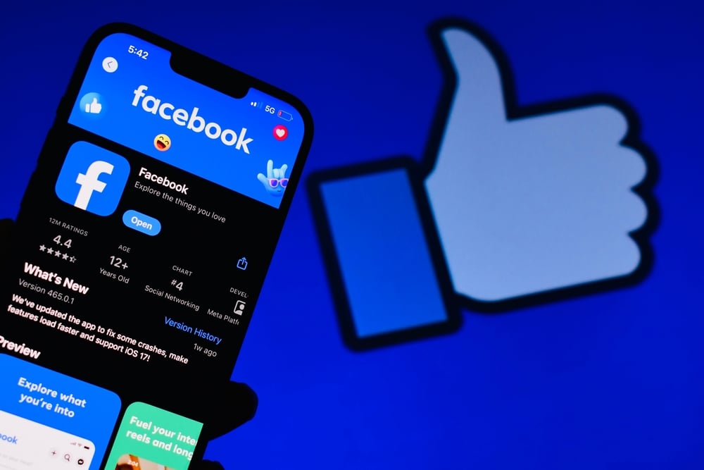 智慧型手機顯示 Facebook 應用程式，背景帶有大拇指圖示。