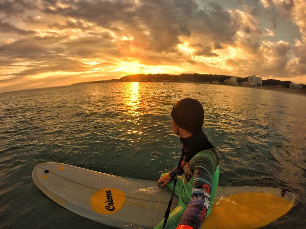 一位衝浪者站在衝浪板上，凝視著海面上金色夕陽的美景。