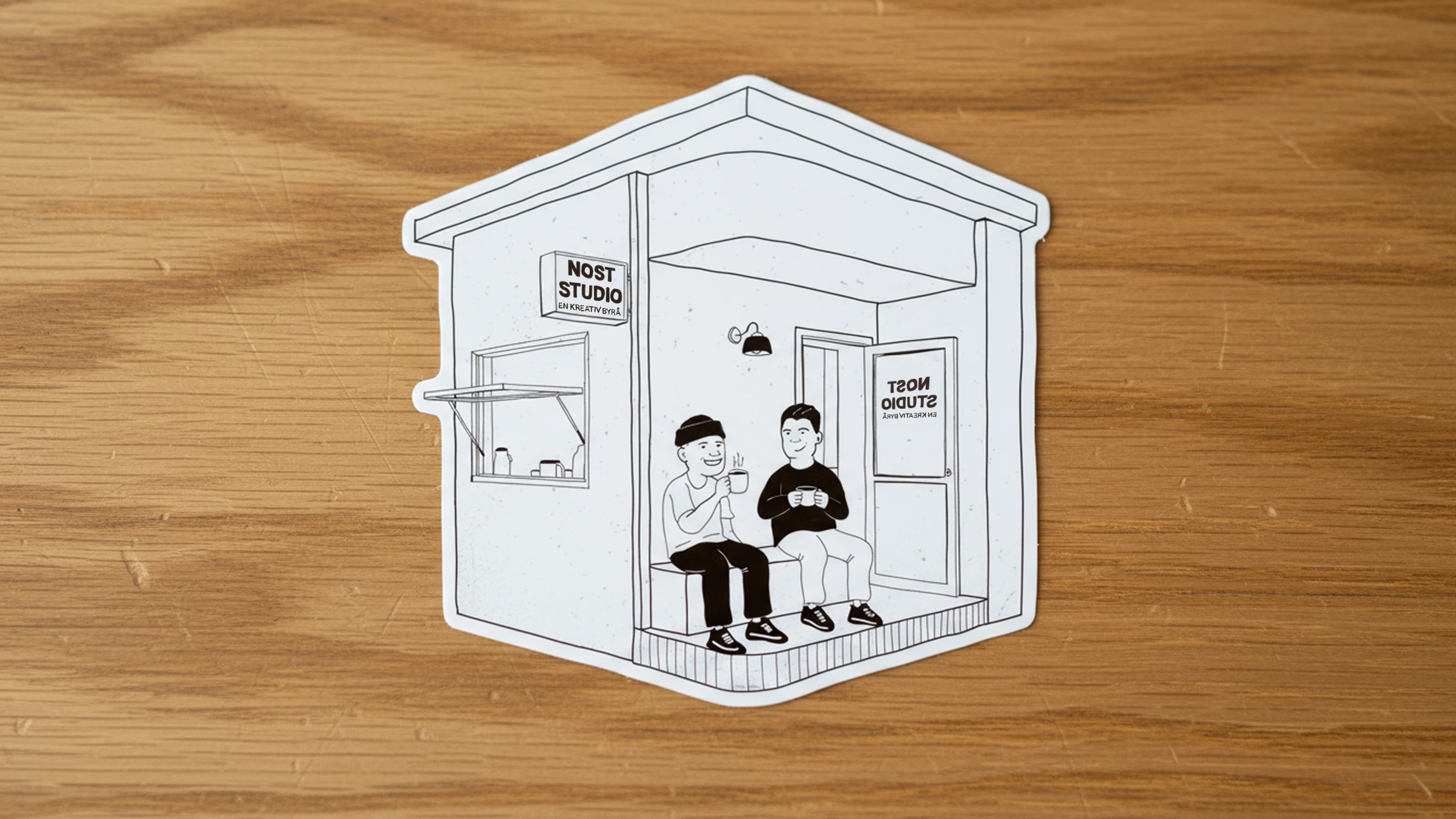 Black and white illustration of two people sitting on a porch drinking coffee outside a small building labeled 'NOST STUDIO'.