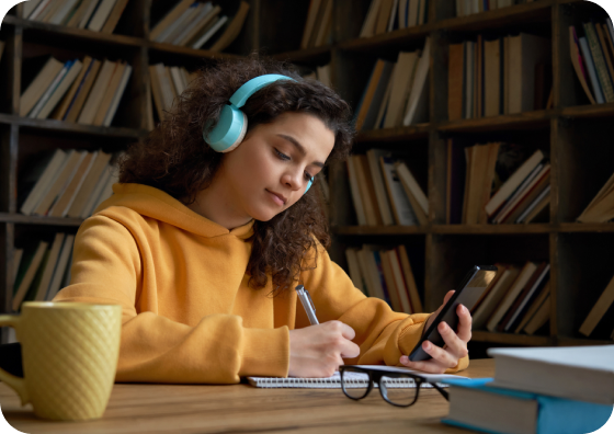 Aluna estudando na biblioteca com celular e anotações