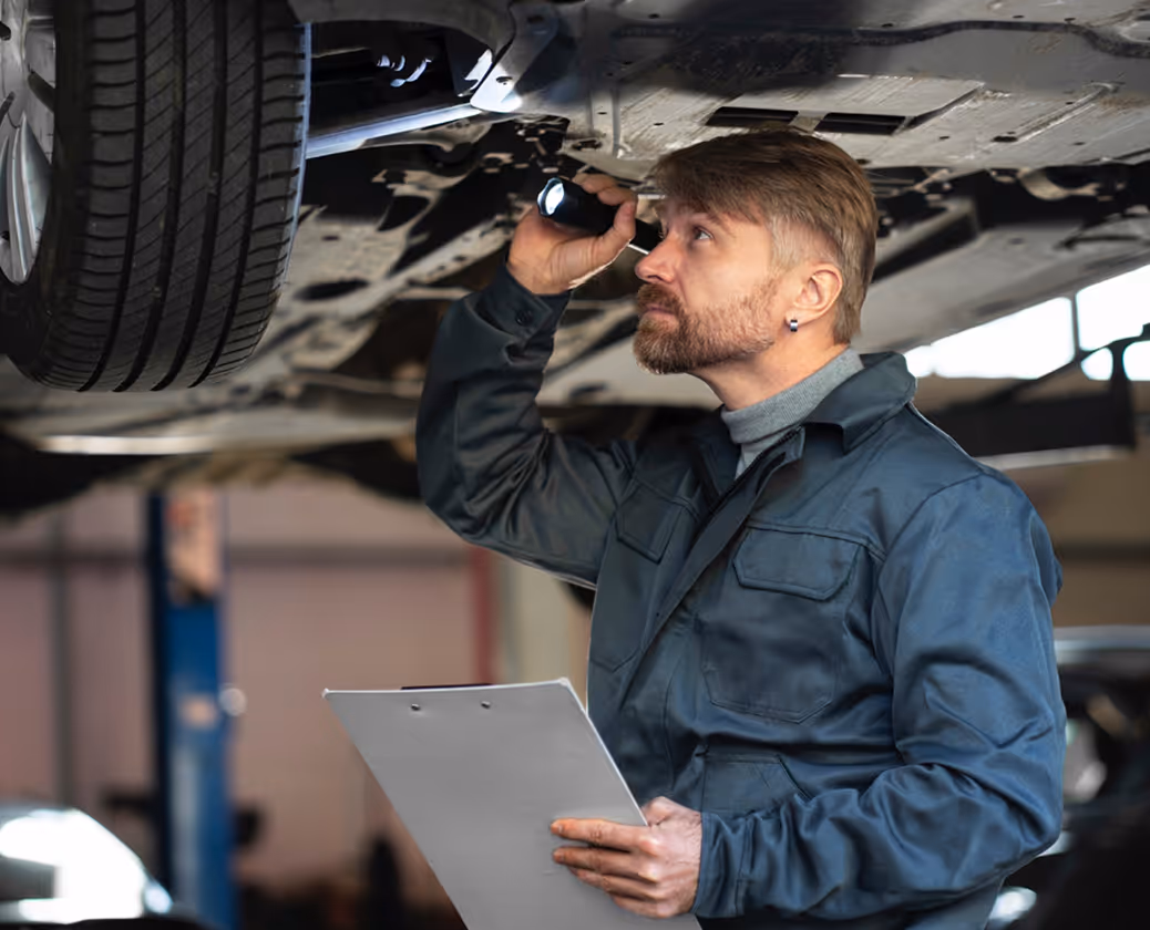 Mechanic inspecting car undercarriage with flashlight and clipboard