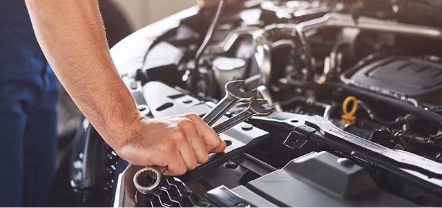 Mechanic using wrench to repair car engine under open hood