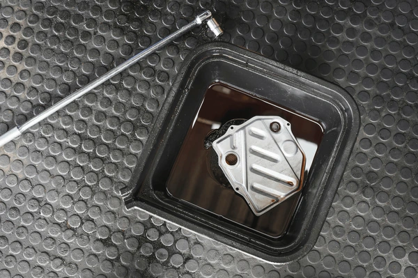 Used transmission filter in oil drain pan with ratchet tool nearby.