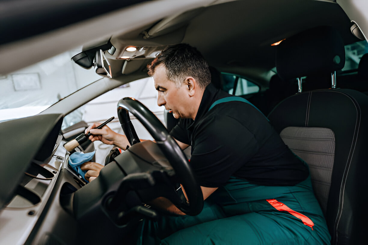 Person fixing car interior, leaning over steering wheel with diagnostic tool