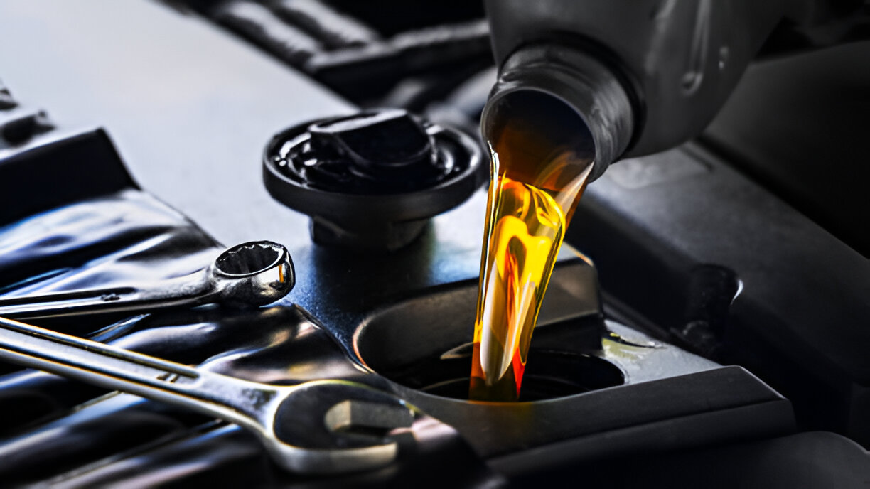 Pouring golden motor oil into engine with wrenches nearby