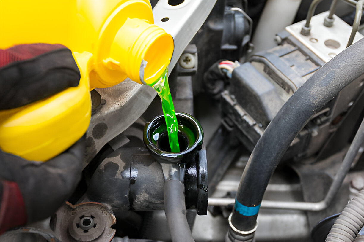 Green coolant being poured into car engine from yellow container