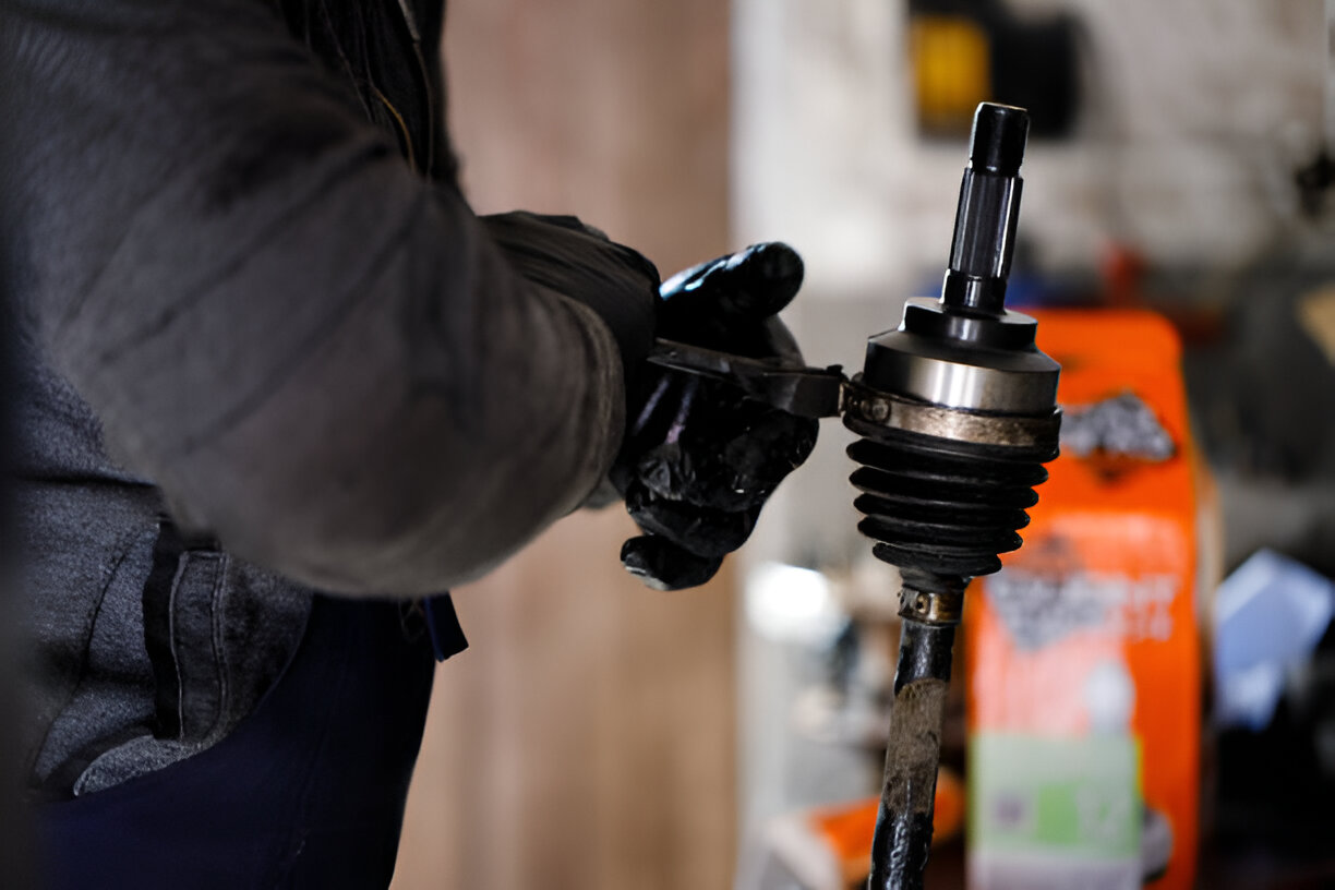 Mechanic's gloved hand working on car's CV joint in workshop