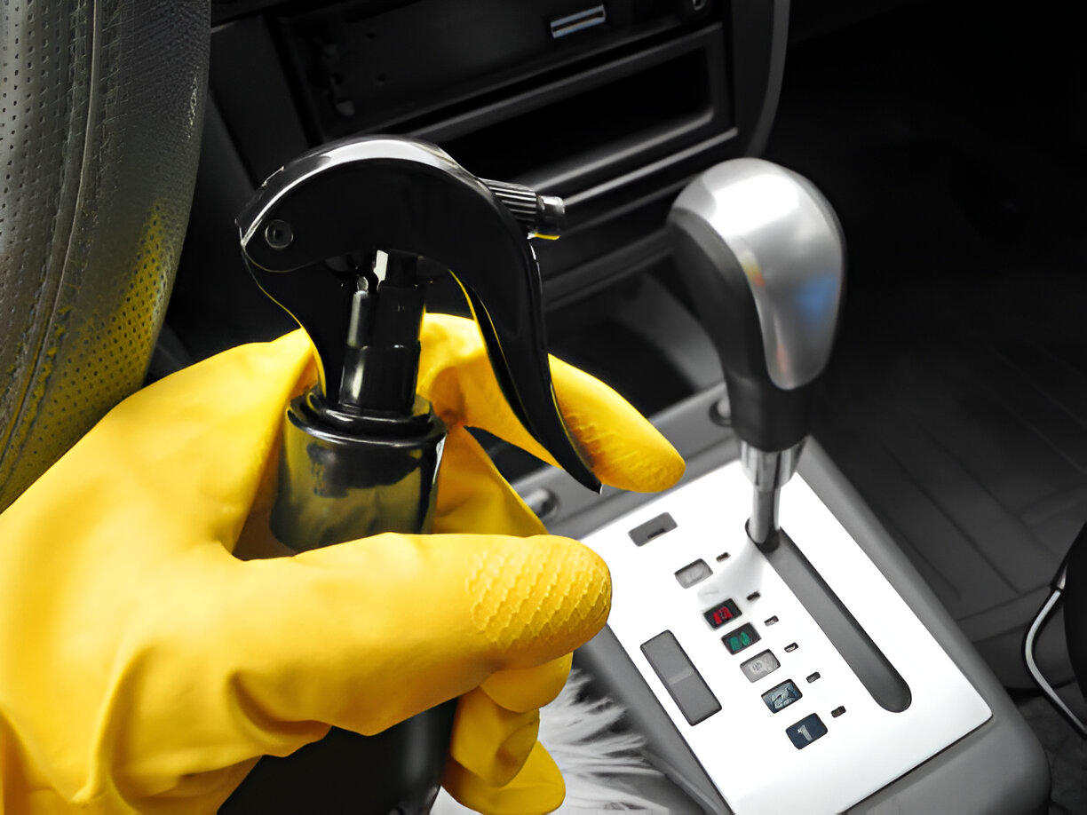 Yellow gloved hand using spray bottle near car dashboard controls