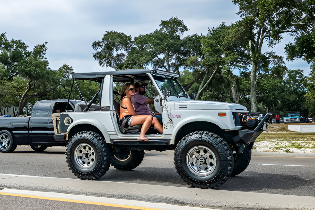 White off-road Jeep with large tires parked on road surrounded by trees
