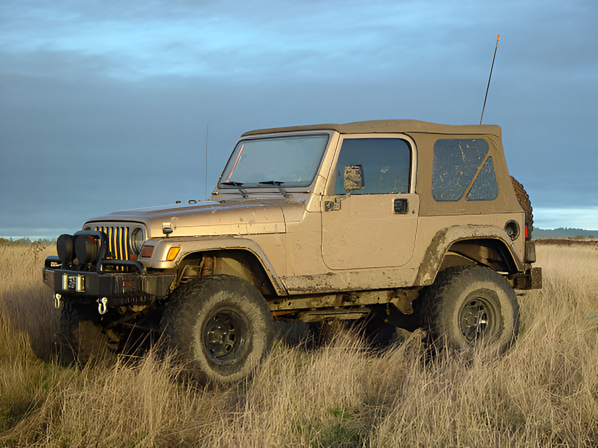 Tan Jeep Wrangler with mud-covered tires parked in dry grassland