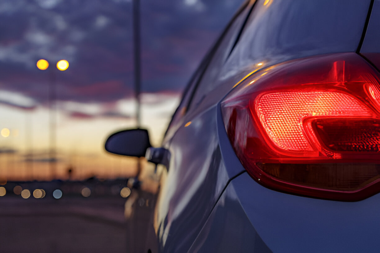 Car tail light glowing red at sunset with blurred city lights background