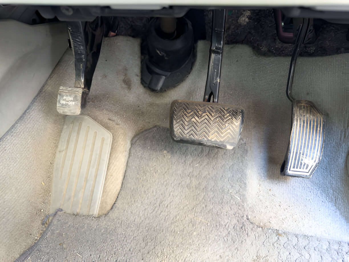 Car floor with gas and brake pedals in dusty interior