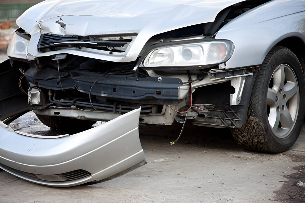 Badly damaged silver car with detached front bumper after a serious collision