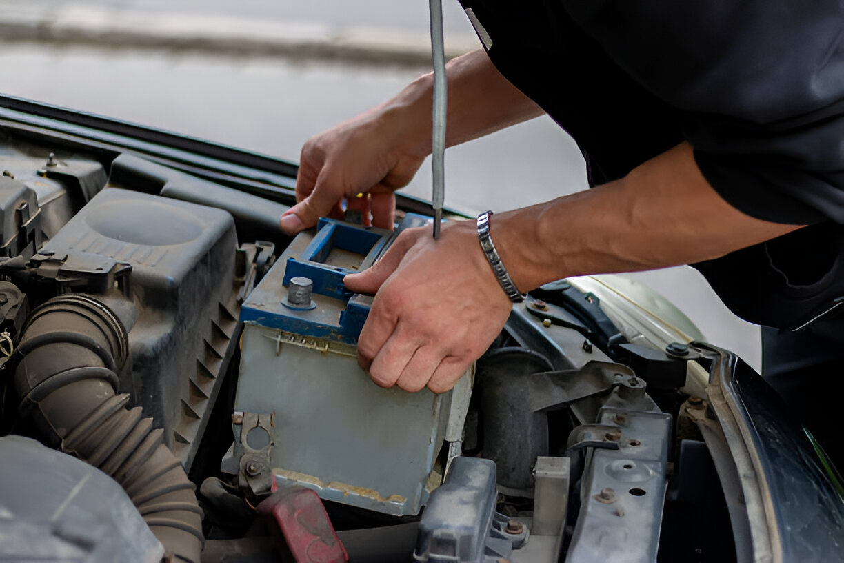 Mechanic's hands working on car battery with wrench under open hood