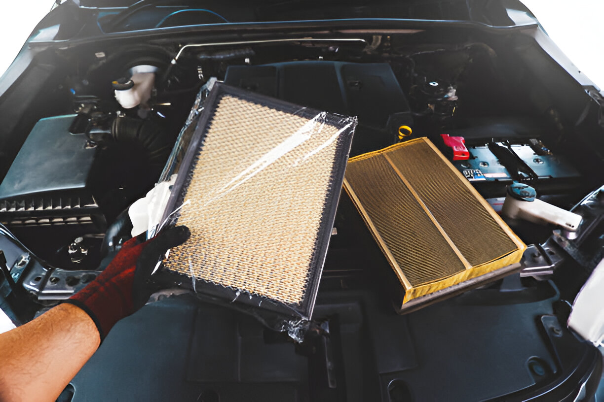 Hand holding two car air filters inside an open vehicle engine compartment
